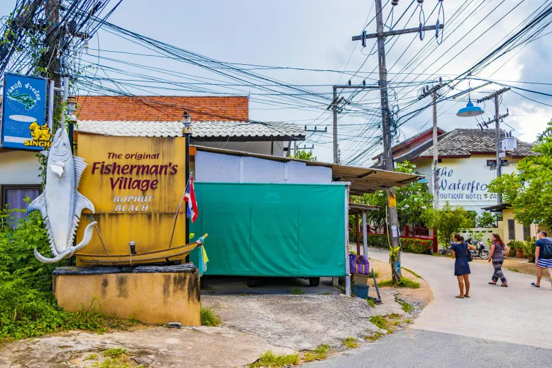 Fisherman's Village sign at a Bophut roadside with walkers and a quiet side road on Koh Samui