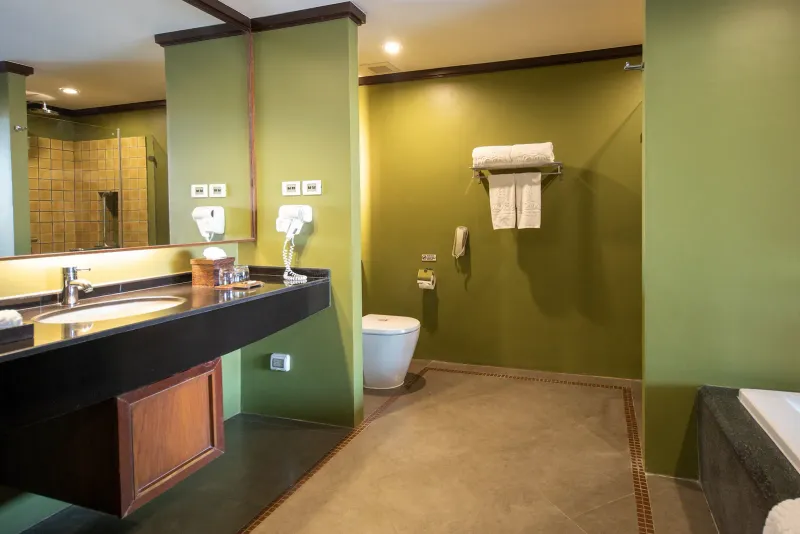 Bathroom in a Nora Buri Resort deluxe room with a bathtub, dark counter and green walls