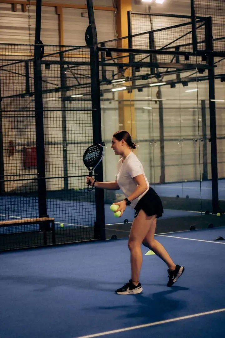 Player holding a padel racket and ball courtside before a coaching session