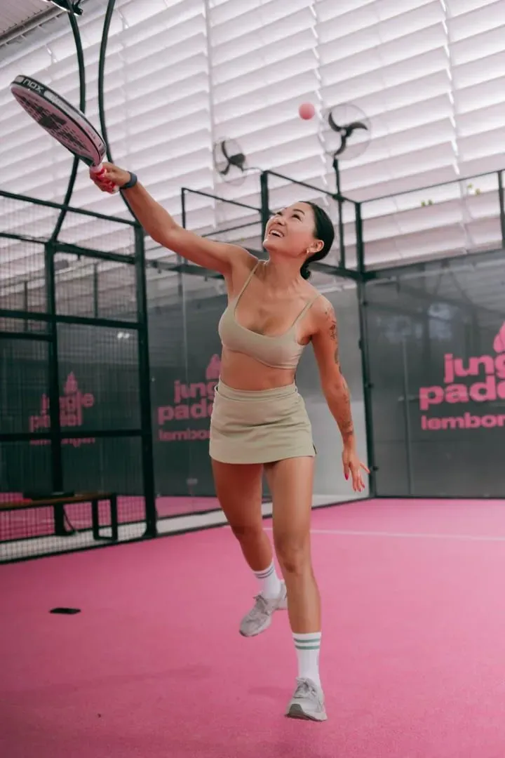 Player reaching for a shot on a pink-toned indoor padel court, the fast-paced style of Padel Samui's covered courts