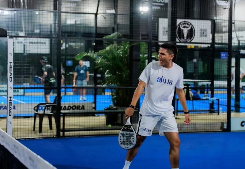 Padel player mid-swing on an indoor court during a fast rally, the Americano-night pace at Padel Samui