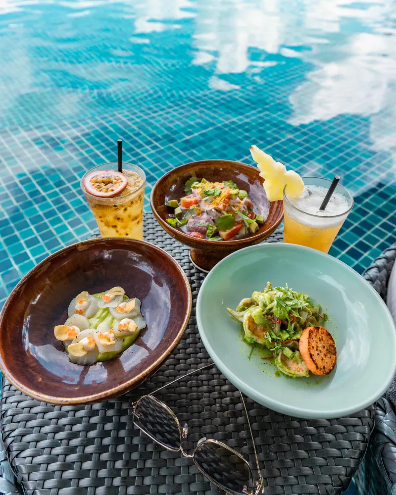 Ceviche, scallop crudo and two fruit cocktails on a poolside table
