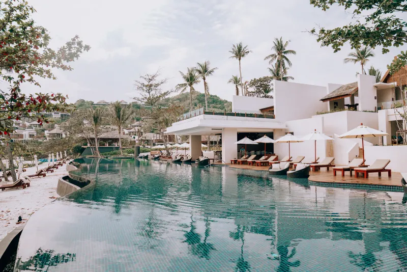 Curving resort pool with a pool bar, loungers and palms beside the beach at The Ritz-Carlton, Koh Samui