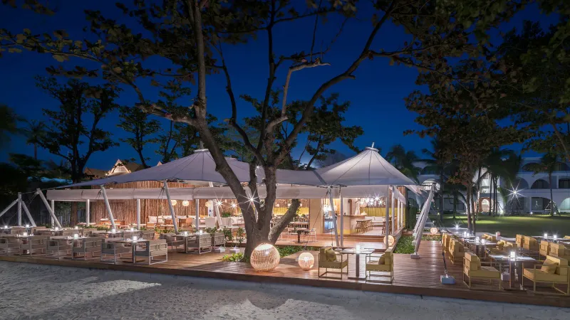 The Tent beachfront restaurant at SALA Samui Chaweng lit at night with white canopies under trees