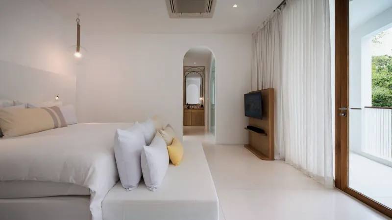Bedroom of a garden two-bedroom family suite at SALA Samui Chaweng with a large bed, white linen and a wall-mounted TV