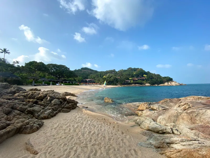 Rocky point and sun loungers along the cove's shoreline, catamaran on the sand