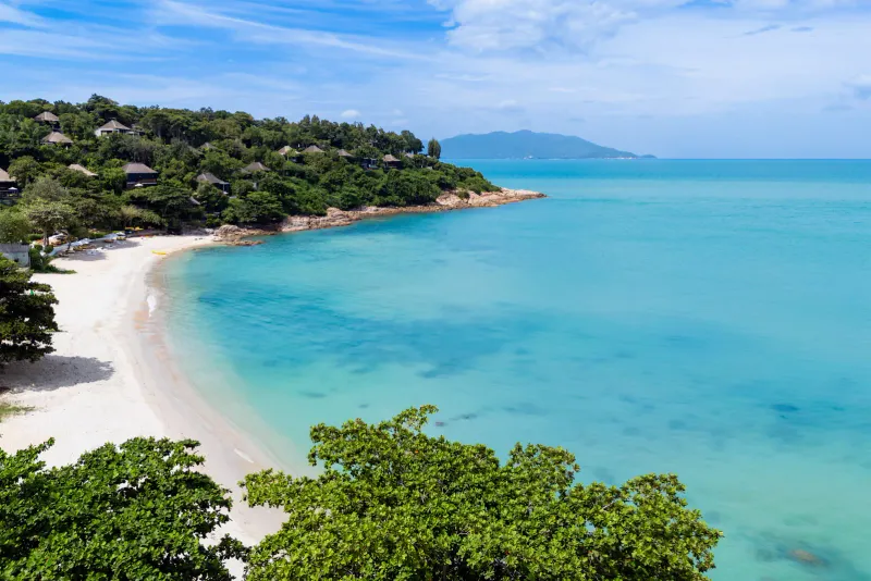 Aerial view of a turquoise cove with hillside resort villas above the sand
