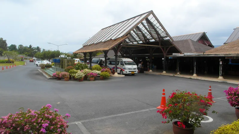 Samui Airport terminal forecourt with minivans under the thatched roof entrance on Koh Samui