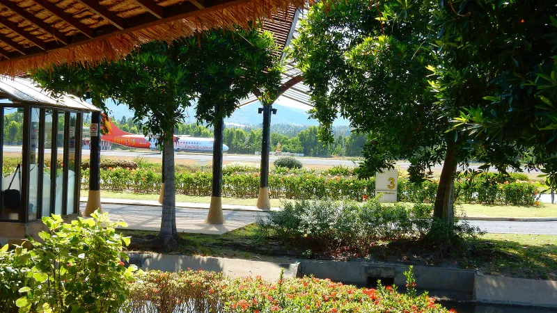Turboprop aircraft taxiing past palms and hedges seen from the open-air terminal at Samui airport