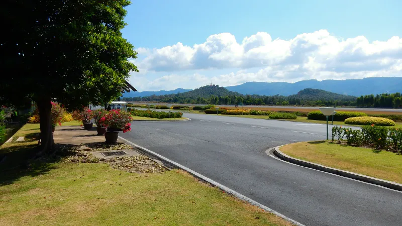 Landscaped road beside the runway at Samui airport with green hills and a hilltop temple behind