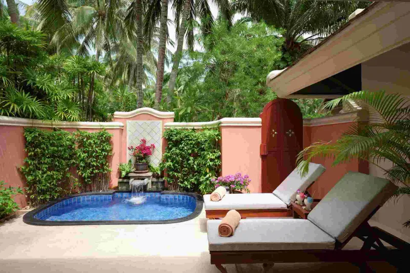 Walled garden plunge pool with small waterfall, loungers and palms at Santiburi Koh Samui