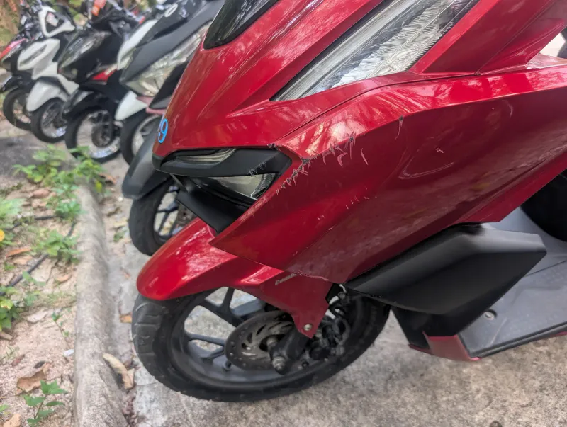 Scratched red scooter front fairing with a headlight surround broken off beside parked bikes