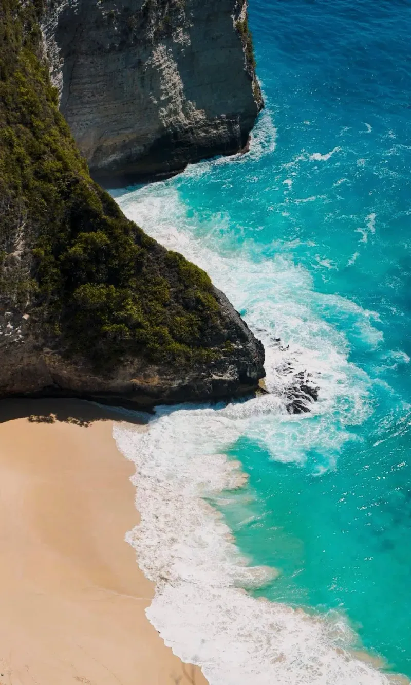 Aerial view of a secluded sandy cove framed by rocky cliffs and turquoise water