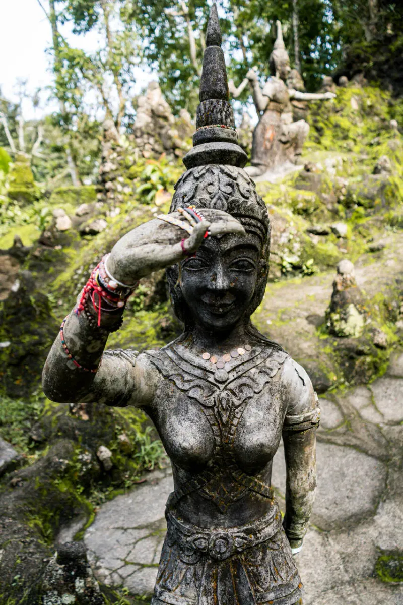 Weathered stone figure with visitor offerings at the Secret Buddha Garden