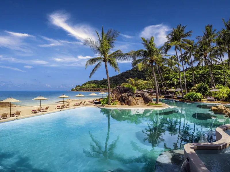 Sheraton Samui Resort infinity pool edge beside the white sand beach with parasols and palm trees