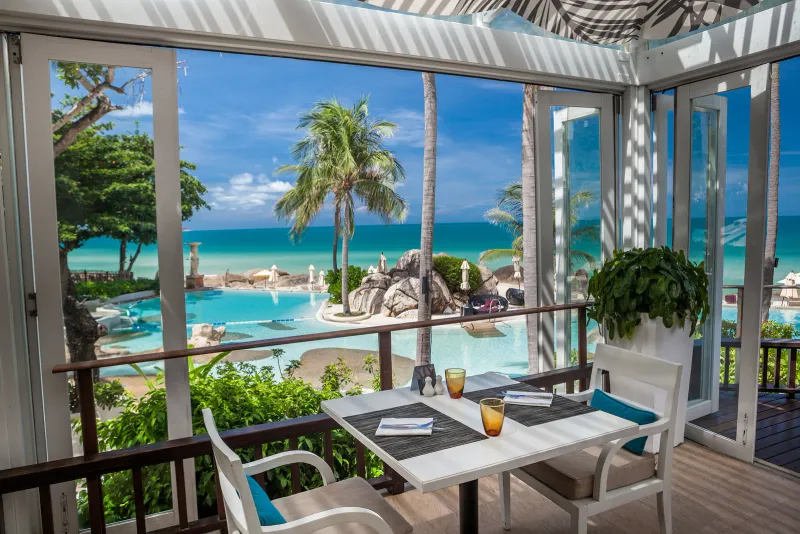 Table for two in an open-fronted restaurant overlooking the pool and sea at Sheraton Samui Resort