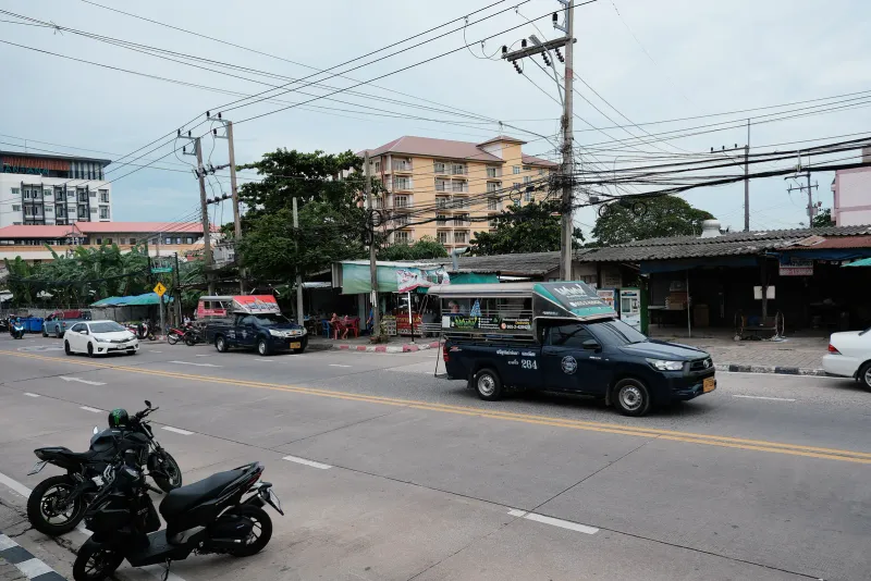 Songthaew pickup truck with a covered passenger bed driving along a Thai town road
