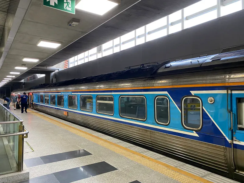 Blue Thai intercity train carriage standing at a station platform with passengers boarding