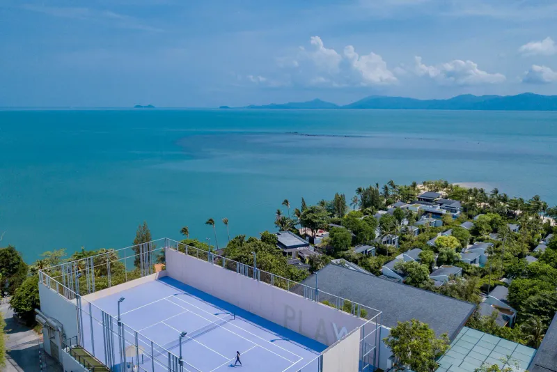 An aerial view of a rooftop court above villas with the sea behind