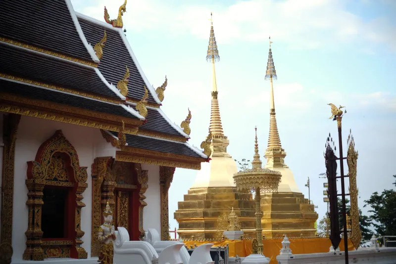 Golden twin chedi spires beside a temple roof with naga finials