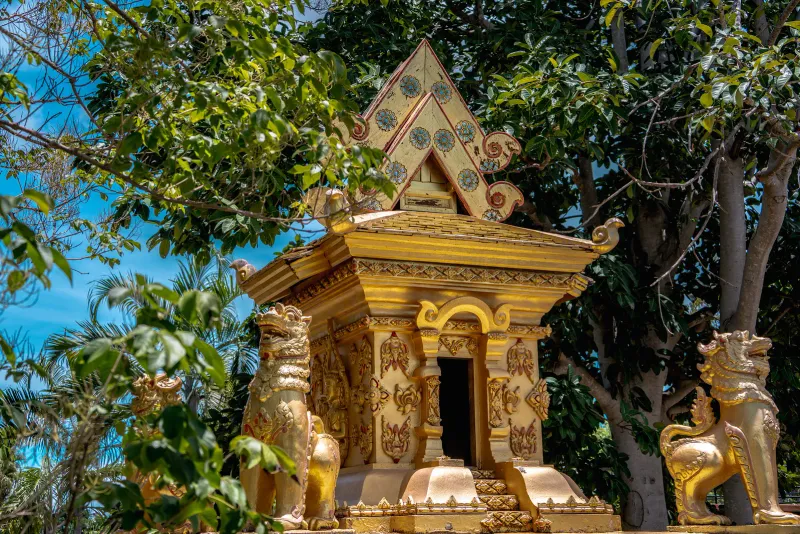Small golden spirit-house shrine flanked by lion guardian statues under jungle foliage