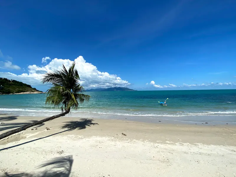 A traditional longtail boat anchored off palm-lined sand with hazy islands on the horizon