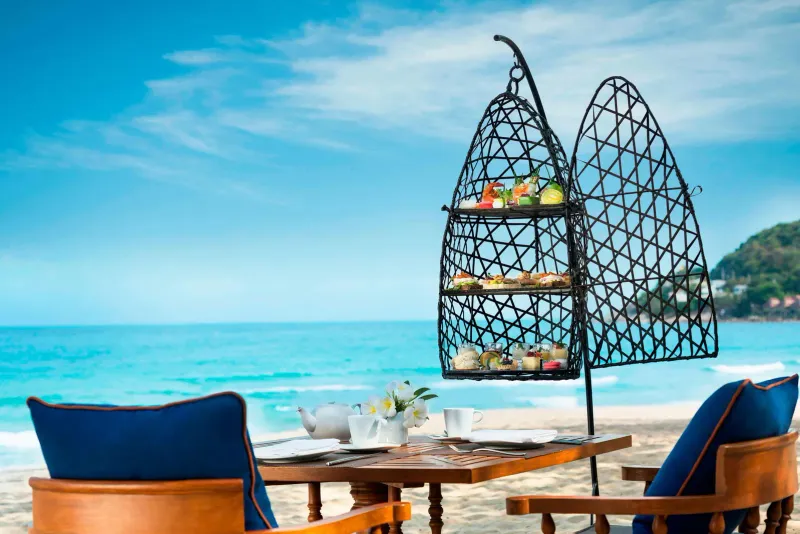 Afternoon tea stand on a beachside table at Vana Belle with turquoise water behind