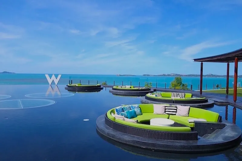 Round green lounges floating in the W Koh Samui reflecting pool with a W logo and the sea behind
