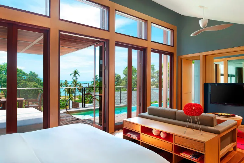 Bedroom and lounge of a W Koh Samui villa with floor-to-ceiling glazing, red accents and a pool terrace