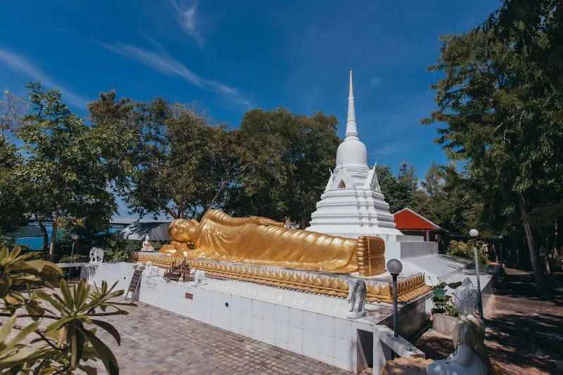 Golden reclining Buddha statue in front of the white chedi at Wat Khao Chedi
