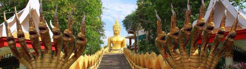 Naga-flanked staircase leading up to a golden Buddha statue on the hillside