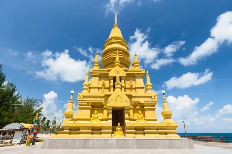 The golden coastal chedi seen from ground level with the sea behind it