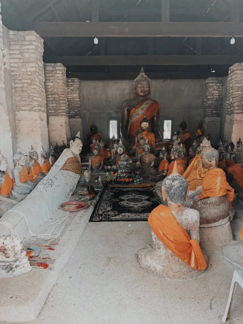 Rows of weathered stone Buddha statues draped in orange cloth inside a temple hall