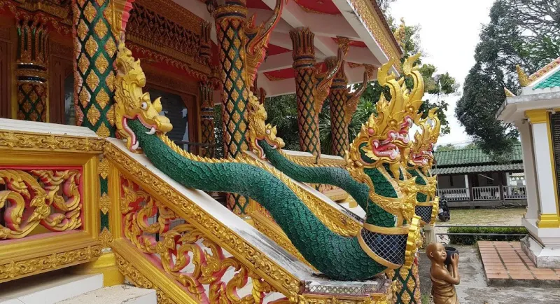 Green and gold naga serpent balustrade lining the temple staircase, with a small novice-monk statue nearby