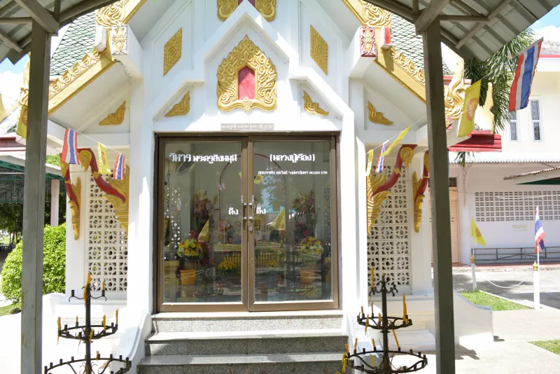 White and gold viharn entrance at Wat Sawang Arom decorated with candle stands and Thai flags
