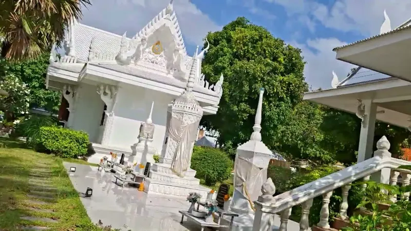 All-white Thai pavilion with tiered gable roof surrounded by palm trees and manicured lawn